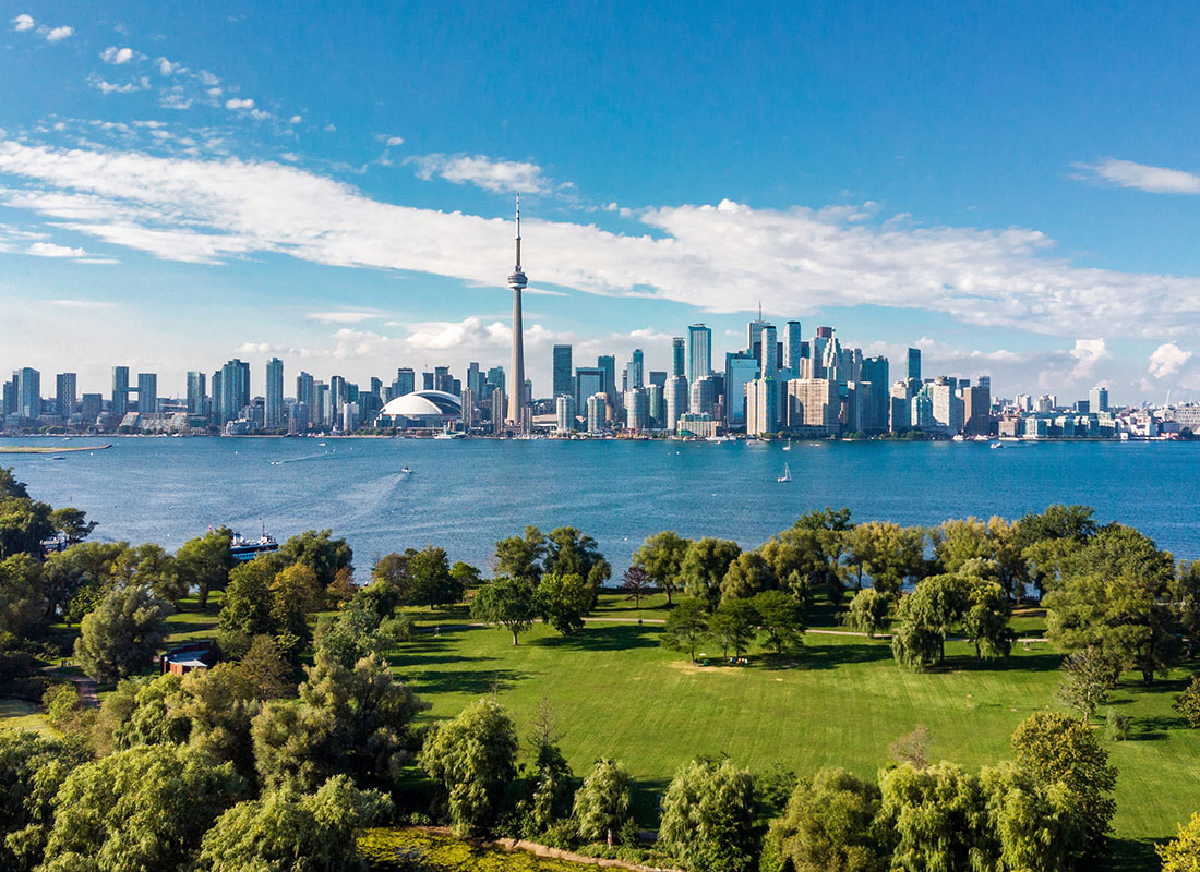 Ontario, BC - Aerial View of Downtown Toronto Skyscrapers Against a Cloudy Blue Sky Next to the Water with Views of a Green Park in Ontario